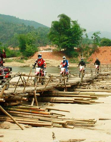 Riders crossing a bamboo bridge in a rural area.