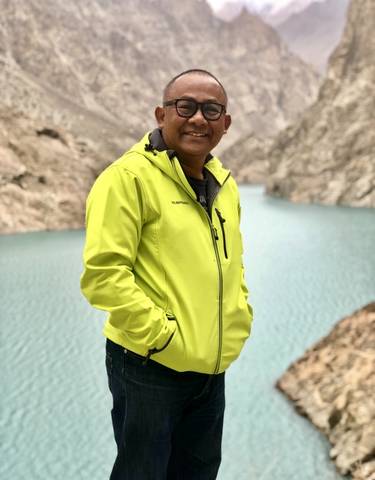 Smiling man in a bright jacket by a turquoise lake.