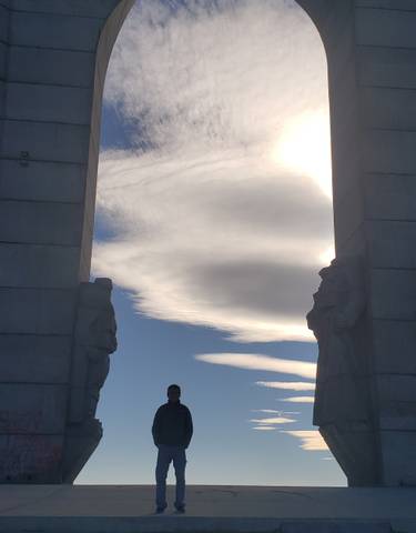 Statues beside towering pillars with clouds in the sky.