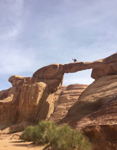 Person standing on a natural rock bridge in a desert setting.