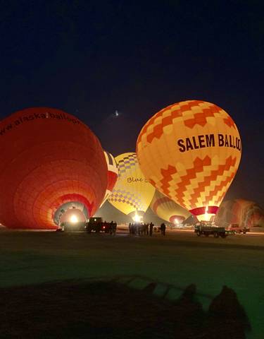 Hot air balloons illuminated at night with a group of people nearby.
