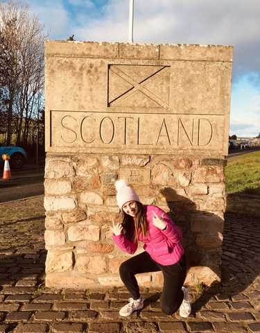 A person posing next to a stone sign marking the Scottish border.