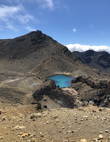 Turquoise alpine lake surrounded by rocky barren hills.