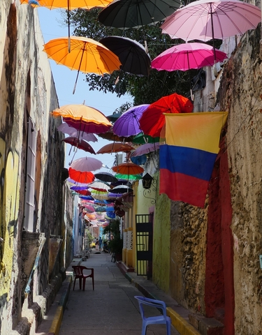 Narrow street decorated with colorful umbrellas and a flag.