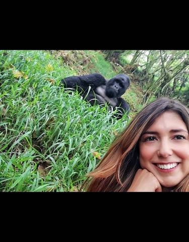 A woman posing with a gorilla in a grassy area.