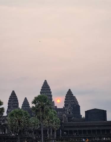 Sunset view of Angkor Wat with the sun between the temple towers.