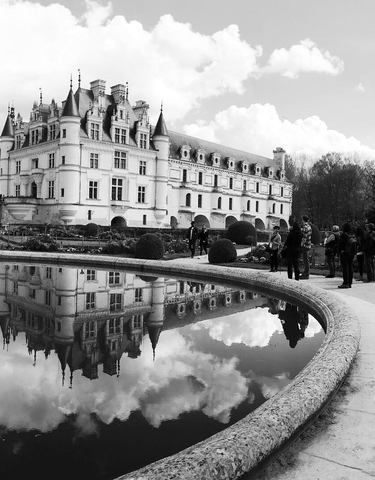 Reflection of a castle in a pond with tourists around.