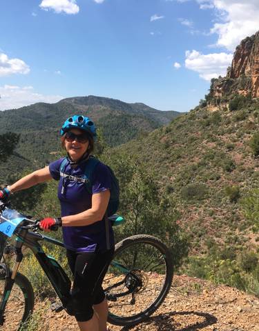 Woman with a bicycle, posing outdoors with mountains in the background.