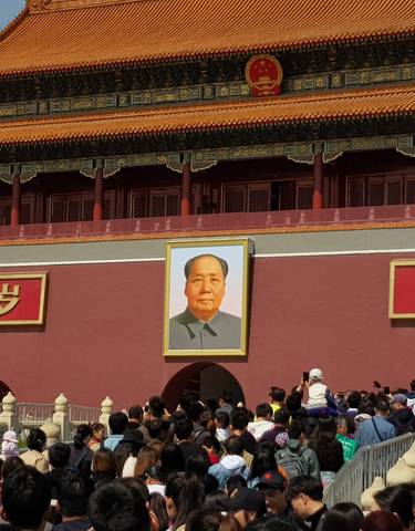 Entrance to a historic site with large portrait and crowds of people.