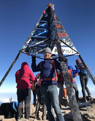 Man standing under the Mount Toubkal summit sign with others around.