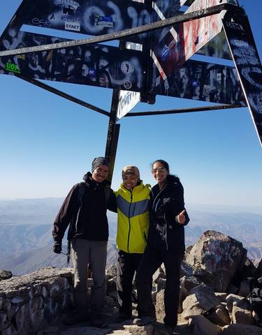 Group of people posing at a mountain summit under a metal monument.