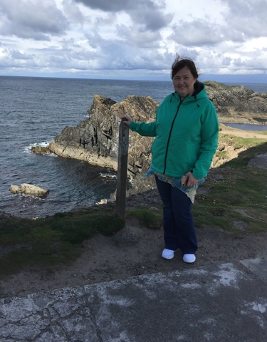 Person standing on a cliff with the sea in the background.