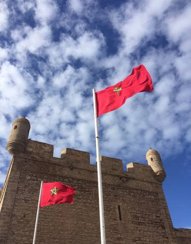 Moroccan flag waving atop a fortified wall under a blue sky.