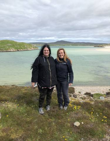 Two women posing by a beach with clear turquoise water.