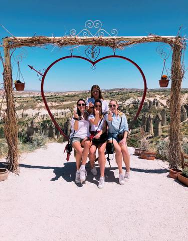 Women sitting on a heart-shaped swing with a scenic view.