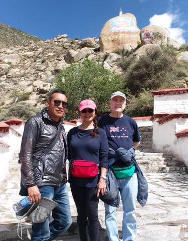 Three people standing outside near steps and rocky landscape.