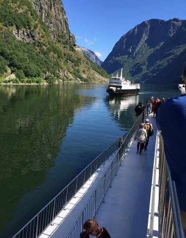 People standing on a ferry with a scenic river view.
