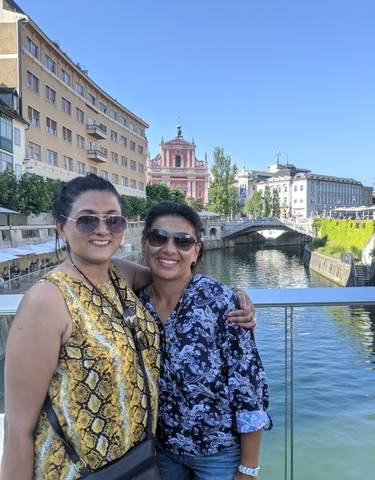 Two women posing on a bridge with scenic architecture in the background.