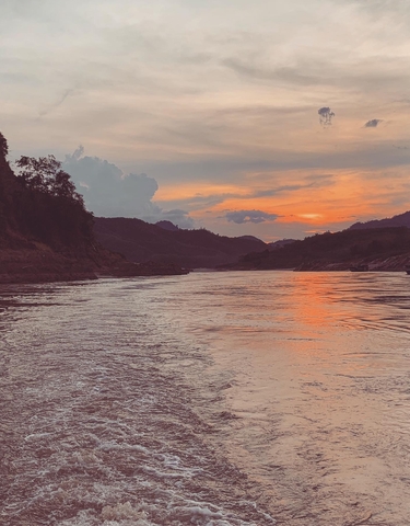 Serene sunset over a river with silhouetted mountains.