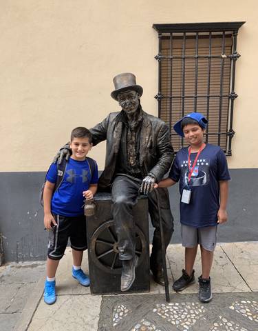 Two children standing with a bronze statue of a man.