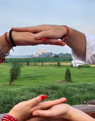 Distant view of the Taj Mahal framed by hands.