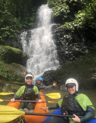 Group of people in front of a waterfall, wearing helmets.