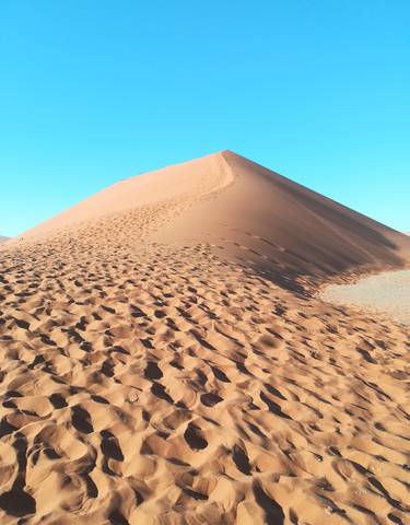 A sand dune in a desert landscape with clear blue sky.