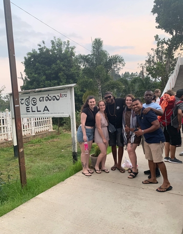 Group at a train station with a sign reading 'Ella'.