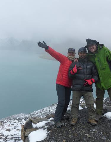 Three people posing by a lake in a mountainous area.