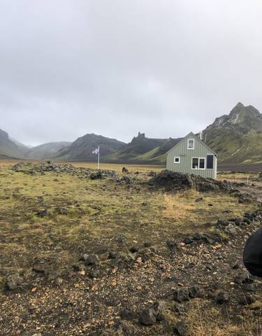 Remote cabin with mountains and a cloudy sky in the background.