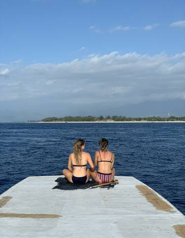 Two people sitting on a boat, ocean and island in background.