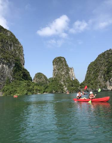 Kayakers paddling in a turquoise bay surrounded by limestone karsts.