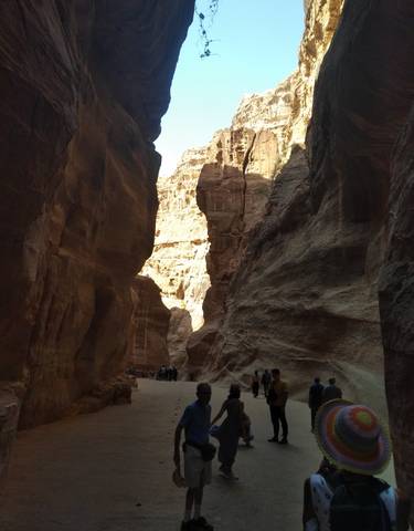 Narrow pathway through towering rocky cliffs with people walking.