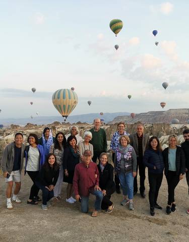 Group of people with hot air balloons in the backdrop.