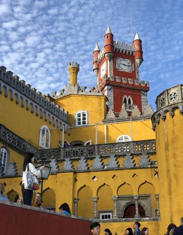 Colorful palace with people on a balcony under a blue sky.