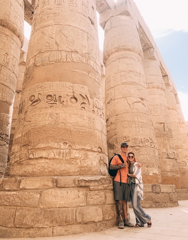 Couple posing in front of ancient Egyptian temple columns with hieroglyphics.