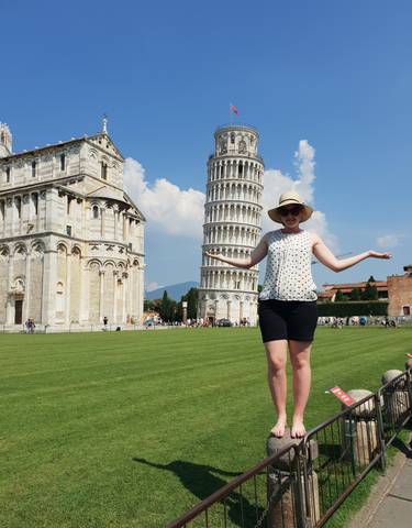 A woman standing in front of the Leaning Tower of Pisa with arms outstretched.