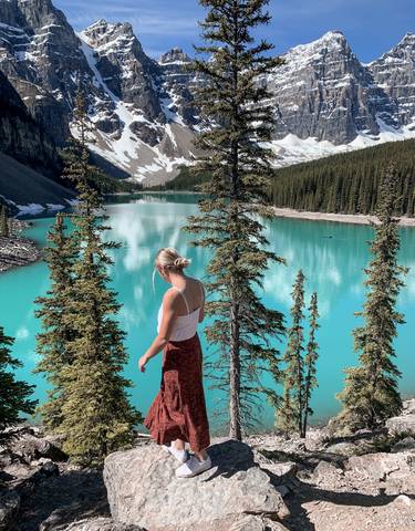 Woman overlooking a turquoise lake with surrounding forest and mountains.