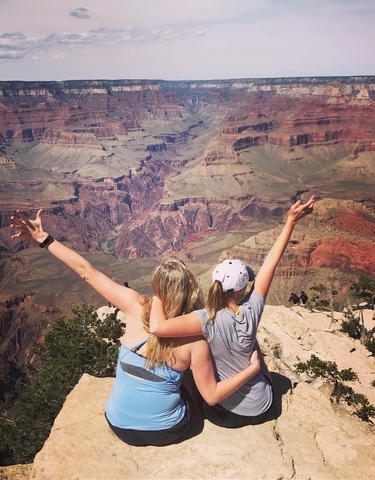 Two people overlooking the Grand Canyon with arms raised.