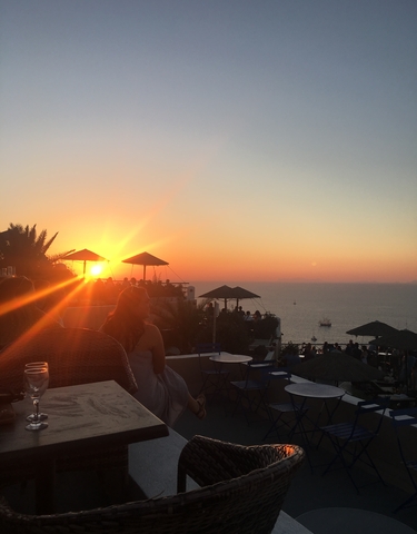 People enjoying a sunset view over the ocean, with patio umbrellas and orange sky.