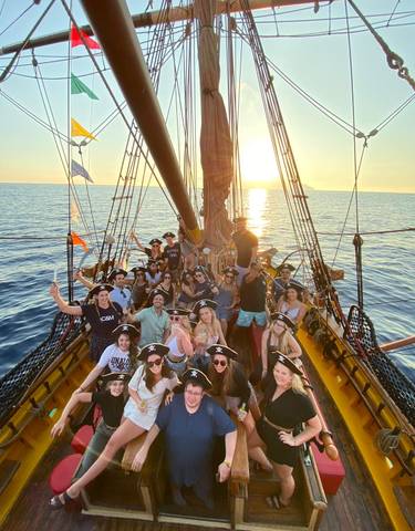 Group posing on a pirate-themed ship at sunset.