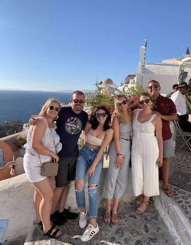Group posing with the sea and traditional architecture in the background.