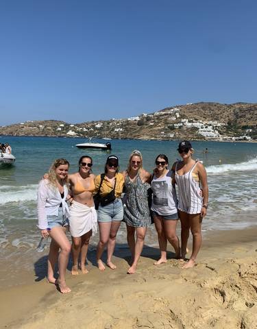 Group of friends posing on a beach with boats and hills.
