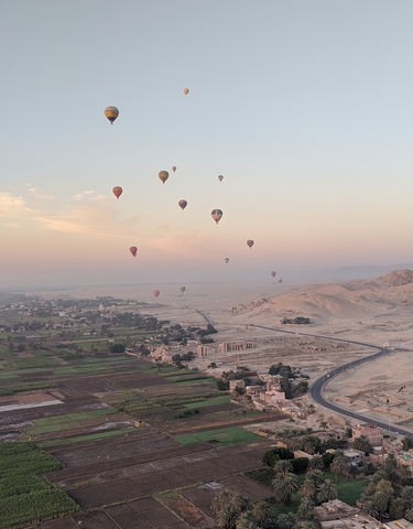 Balloons floating over a landscape with distant hills and a sunrise.