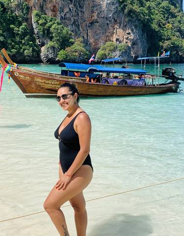 Woman standing in shallow water with a traditional boat in the background.