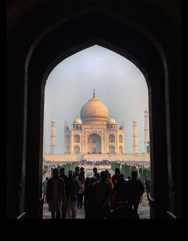 Daylight view of the Taj Mahal framed by an archway with visitors in the foreground.