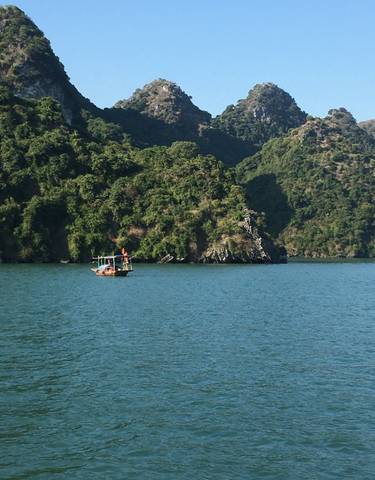 Small boat on a lake surrounded by lush green hills.