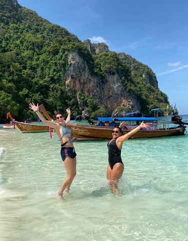Two women posing in water with a traditional boat in the background in Thailand.
