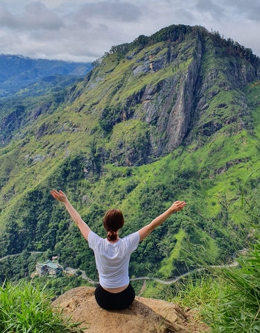 Person with arms raised facing a lush green mountain landscape.