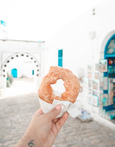 Close-up of a doughnut against a picturesque alley with bright blue doors.